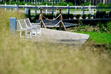 A wooden bench is on a boardwalk with a fence and trees in the background.