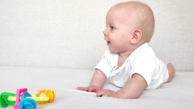 Funny baby laughs and plays with a rattle on a white blanket, baby's morning