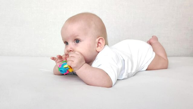 Funny baby laughs and plays with a rattle on a white blanket, baby's morning