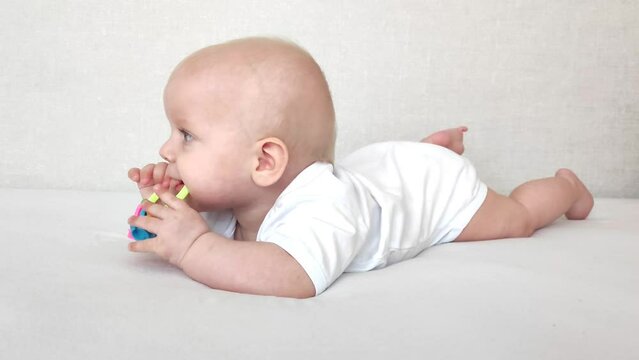 Funny baby laughs and plays with a rattle on a white blanket, baby's morning