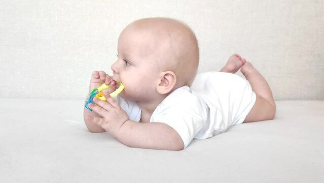 Funny baby laughs and plays with a rattle on a white blanket, baby's morning