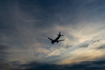 Fototapeta na wymiar Silhouette of an airplane against the cloudy sky in the fading evening light