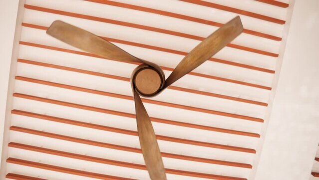 Wooden ceiling fan gracefully spinning in a circular motion. The elegant motion of the blades creates a cooling breeze while adding a touch of rustic charm to any interior . High quality 4k footage