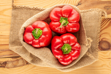 Three sweet red peppers in a jute bag on a wooden table, macro, top view.