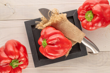 Three sweet red peppers with a knife on a wooden black tray on a wooden table, macro, top view.