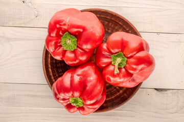 Three sweet red peppers with clay plate on wooden table, macro, top view.
