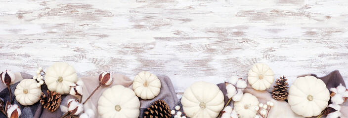 Cozy autumn bottom border with blanket, white pumpkins natural decor. Top down view over a white...