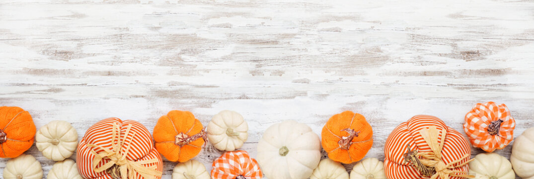 Autumn farmhouse pumpkin bottom border over a white wood banner background. Rustic orange and white cloth pumpkins. Top view with copy space.