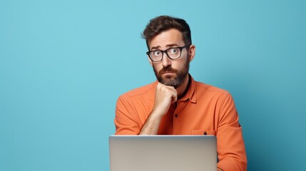 Portrait of a confused puzzled minded African American man in orange top with laptop isolated on blue background, with copy space. - obrazy, fototapety, plakaty