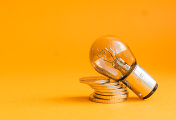 A lamp and money on a orange
 background with copy space. Price for electricity concept. Expensive electricity cost. - obrazy, fototapety, plakaty