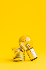 A lamp and money on a yellow background with copy space. Price for electricity concept. Expensive electricity cost. - obrazy, fototapety, plakaty