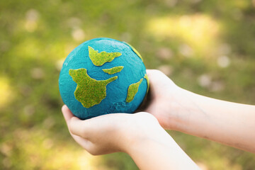 Young boy's hand holding planet Earth globe at natural park background as Earth day to save this planet with ESG principle and environment friendly energy for brighter future. Gyre