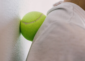 Closeup young woman shoulders in tight top leaning on small yellow tennis ball against wall to fix...