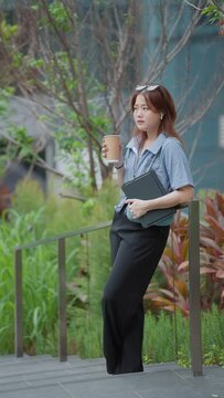 Young asian woman talking on smartphone with friend rejoicing smiling holding tablet at outdoors. Young businesswoman or university studen talking on smartphone at city view. Vertical