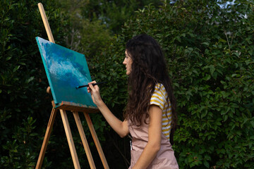 Woman painting a blue abstract art picture on an easel in nature