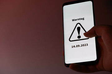 Symbol for the national warning day in Germany, 2022. Hand holds a mobile phone with the German text "Warntag 8. Dezember" (warning day on December 8th).