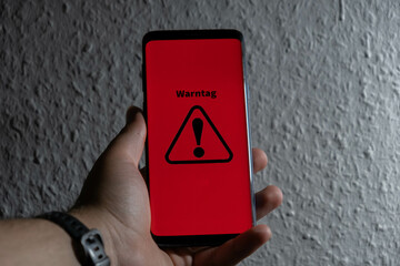 Symbol for the national warning day in Germany, 2022. Hand holds a mobile phone with the German text "Warntag 8. Dezember" (warning day on December 8th).