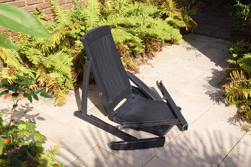 Broken plastic black-gray garden chair. Collapsed. Dutch garden, summer, September.
