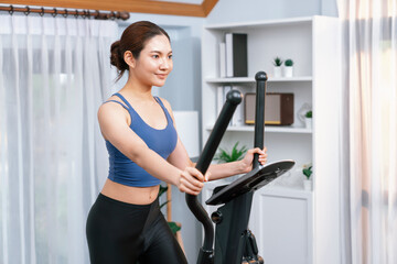 Energetic and strong athletic asian woman running on elliptical running machine at home. Pursuit of...