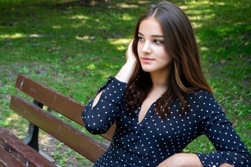 Emotional girl teenager with long hair hairstyle braids in a green shirt sits on a bench in the park. High quality photo