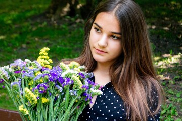 Emotional girl teenager with long hair hairstyle braids in a green shirt sits on a bench in the park. High quality photo