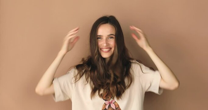 Lovely coquettish brunette curly woman, winking playfully, flirting. Woman fix her hair on beige background. Lovely coquettish brunette woman, playfully flirting.