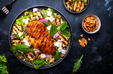 Gourmet salad with zucchini and grilled chicken, feta cheese, walnut, onion and spinach, black table background, top view