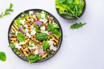 Delicious healthy salad with grilled zucchini, feta cheese, walnut, onion and spinach, white table background, top view