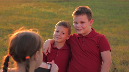 Happy little brothers pose to girl taking photo with camera in sunset park