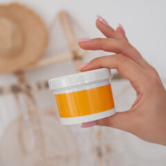 girl holding a yellow jar of cream against the background of a summer beach house