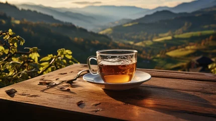 Poster Hand holding a cup of hot tea and natural view of the mountain landscape at the time the sun appears © MBRAMO