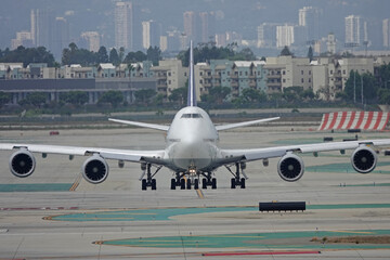 A large passenger airliner jet is shown from the front, taxiing at a large airport during the day.
