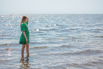 Fototapeta na wymiar Beautiful young blonde girl looking at calm sea and blue sky. Side view. High quality photo