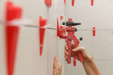 Woman tiling bathroom walls. Flat wall plastic tile leveling system. Process of installation of...