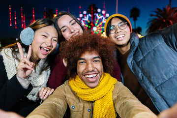 Young happy diverse group in winter clothes taking selfie portrait outdoors. Multiracial people having fun on christmas vacation. Friendship and travel concept. - Powered by Adobe