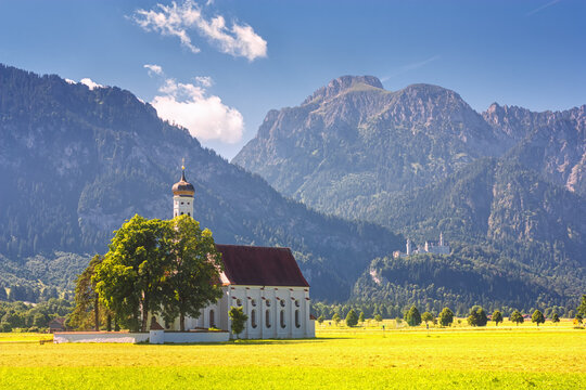 Bavarian landscape - view of the church of St. Coloman on the background of the Alpine mountains and Neuschwanstein Castle in summer day, Germany