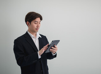 Business man portrait Asian one person wearing a black suit, handsome cool sharp smart standing looking, hand holding mobile phone and tablet ready for work inside the office, with white background
