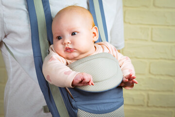 Portrait of a cute little baby girl in a sling looking at the camera.