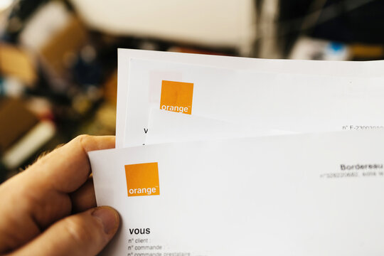 Paris, France - Mar 27, 2023: A first-person perspective shows a male hand gripping an Orange Telecom paper invoice adorned with the distinctive square logo