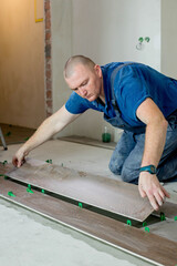 Tiler placing ceramic wall tile in position over adhesive with lash tile leveling system. Ceramic Tiles.