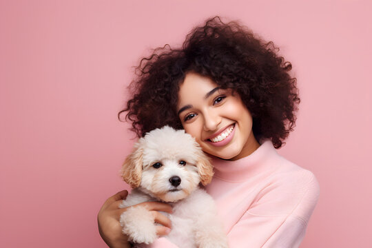 Happy Young Woman With Curly Hair Hugging Cute Puppy, Smiling As Pet Owner Holding Dog With Love And Care In Studio, Isolated On Pink Background