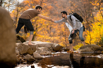 Friend giving a helping hand while crossing the stream barefooted walking by the creek with his...