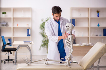 Young male doctor with skeleton in the clinic