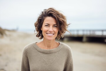 Portrait photography of a French woman in her 40s wearing a cozy sweater against a beach background