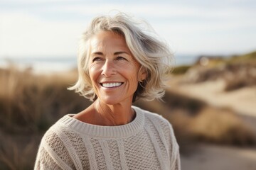 Portrait photography of a French woman in her 60s wearing a cozy sweater against a beach background