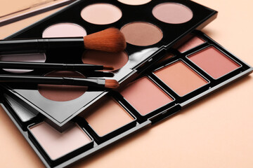 Colorful contouring palettes with brushes on beige background, closeup. Professional cosmetic...