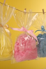 Packaged sweet cotton candies hanging on clothesline against yellow background