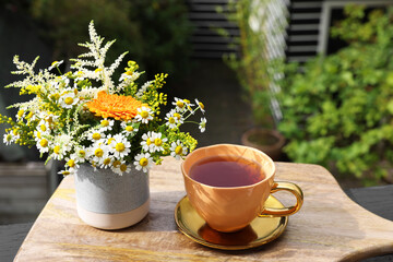 Cup of delicious chamomile tea and fresh flowers outdoors on sunny day