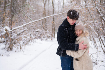 Fototapeta na wymiar A young couple walks in the park in winter. Guy and girl hugging outdoors.