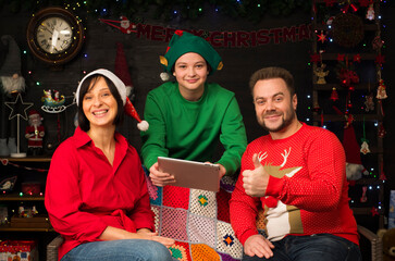 family against the background of Christmas decoration uses a tablet recommends something. father, mother and son with a tablet in a Christmas atmosphere. online shopping concept